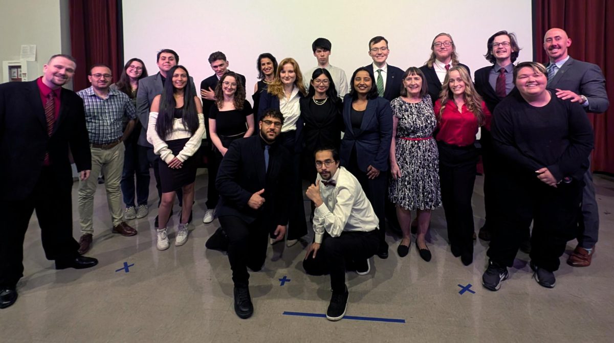Group of 21 people dressed in formal and semi-formal attire posing together in front of a screen.