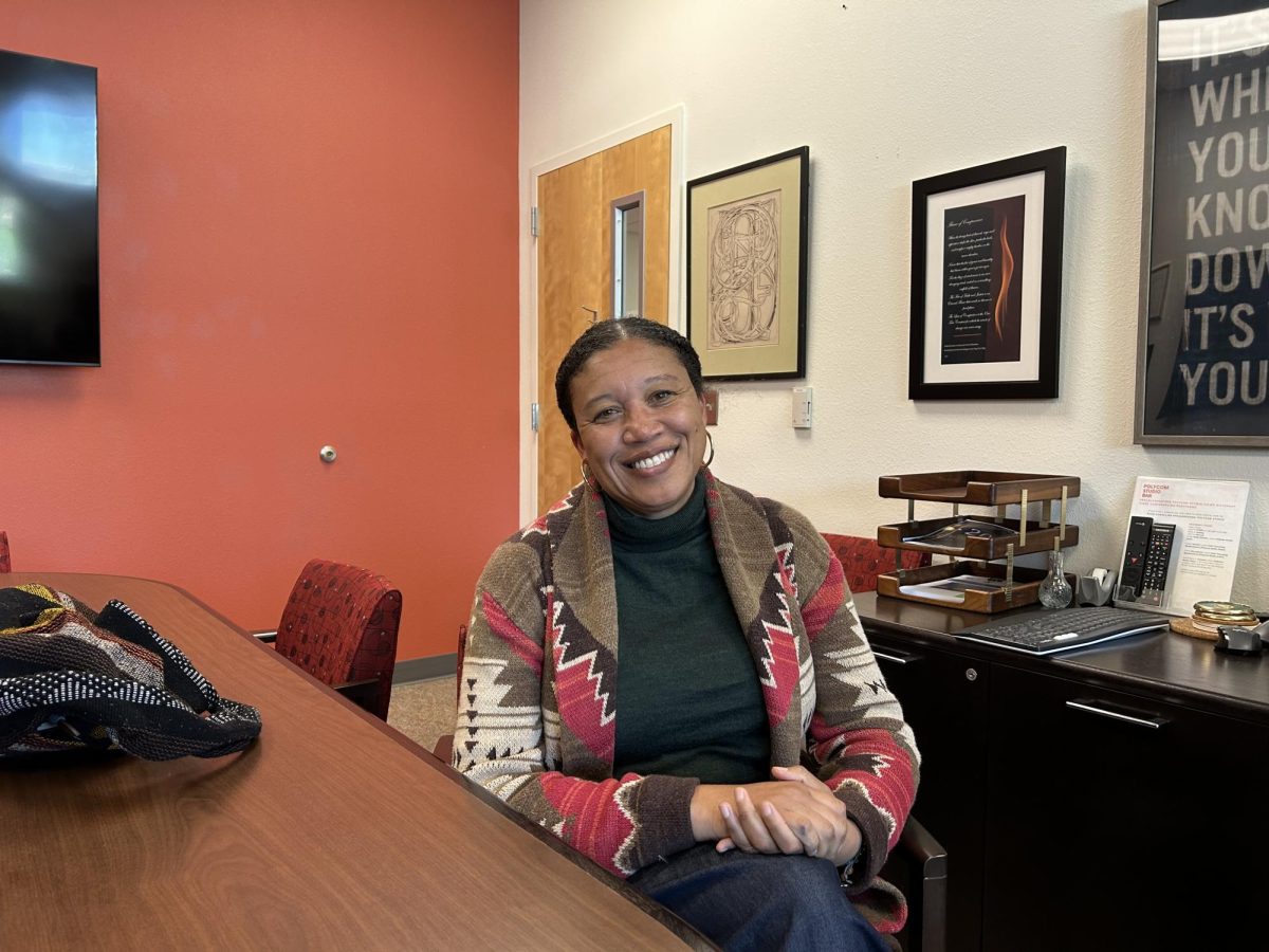 Grossmont President seated at a desk in an office with red and white walls and framed art on display.