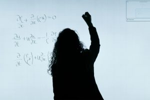 Person writing complex mathematical equations on a large whiteboard or screen.