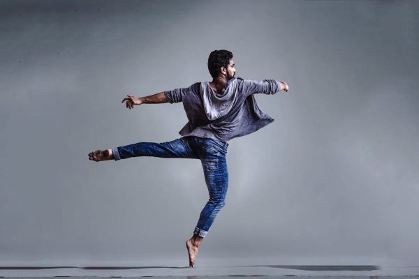 Man balancing on one foot with extended arms and leg in a contemporary dance pose.